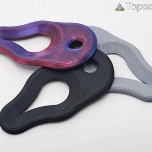 May include: Three teardrop-shaped objects with a central cutout and a small circular hole at one end. One object features a gradient of purple and blue, one is solid black, and one is solid light gray. Each piece has a textured, ridged surface.