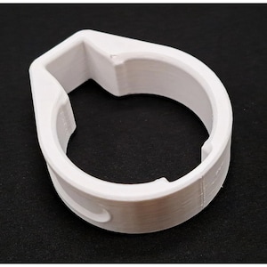 May include: A white, 3D-printed circular component featuring a tapered, angular top section and a hollow centre. The object has a smooth, matte finish with visible layer lines along its curved exterior walls and a distinct, notched inner rim.