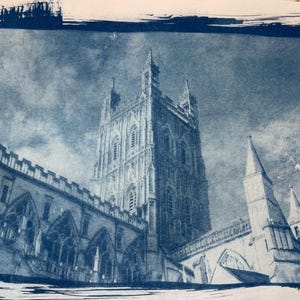 Op de afbeelding: Blauw getinte architecturale prent van een kathedraal, met een hoge centrale toren met ingewikkelde details en meerdere torens. De afbeelding heeft een vintage esthetiek, met een donkerblauwe rand en een bewolkte lucht.