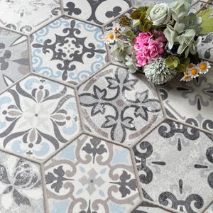 May include: Hexagonal tiles with a vintage design in shades of gray, blue, and white. The tiles feature intricate floral and geometric patterns. A bouquet of pink, white, and green flowers rests on the tiles.