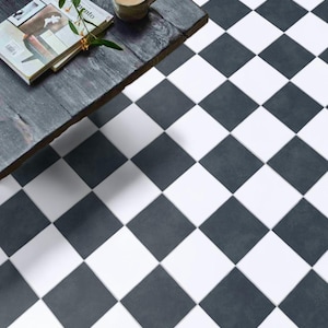 May include: A high-angle shot of a black and white checkered tile floor. A dark wooden table with a coffee cup and a magazine is in the upper left corner. The floor tiles are square and arranged in a classic checkerboard pattern.