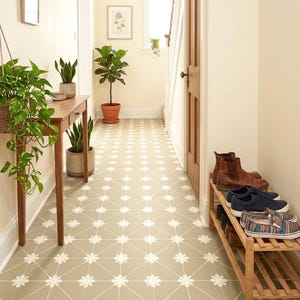 May include: A hallway with light beige walls and a floor featuring a white floral grid pattern. A wooden console table holds a hanging plant and a potted snake plant. A wooden shoe rack displays brown leather boots, blue sneakers, and patterned slip-ons.