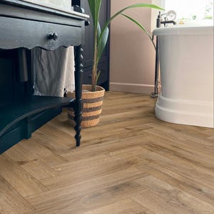May include: Light brown wooden flooring laid in a herringbone pattern. The floorboards are arranged in a repeating V-shape design. The flooring is in a bathroom with a black vanity, a white bathtub, and a potted plant.