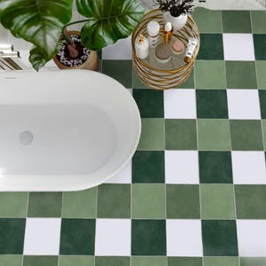 May include: A modern bathroom featuring a white oval bathtub, green and white chequered tile flooring, and a small gold side table with beauty products. A potted plant with large green leaves is also visible.