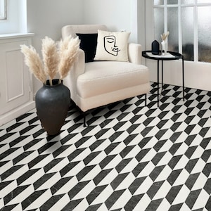 May include: A black and white geometric patterned floor tile with a white armchair and a black side table with a vase of dried pampas grass.