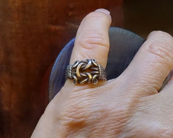 May include: A silver ring with a twisted design, featuring a central knot with a gold accent.