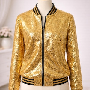 Puede incluir: Chaqueta bomber dorada con lentejuelas, cremallera negra y ribete a rayas negras y doradas en el cuello, los puños y el dobladillo. La chaqueta se exhibe en un maniquí. La chaqueta es una prenda de abrigo glamurosa.