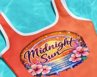May include: Orange swimsuit with white trim and the words "Midnight Sun" in a decorative font. The swimsuit features a graphic of a sunset and hibiscus flowers. The background is a light blue water.