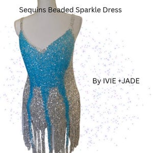 May include: A sleeveless dress featuring a V-neckline, adorned with silver and bright blue sequins and beads. The garment includes a fringe hemline and displays the text Sequins Beaded Sparkle Dress By IVIE + JADE on a white background.