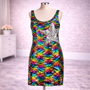 May include: A multi-coloured sequin dress on a mannequin. The dress has a silver sequin star on the front. It has a scoop neckline and a straight hemline that falls to the knees. The dress is sleeveless and would be suitable for a party.