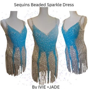 May include: A sleeveless dress featuring a V-neckline, covered in silver and bright blue sequins and beads. The garment has a fringe hemline and displays the text Sequins Beaded Sparkle Dress By IVIE +JADE at the top and bottom of the image.