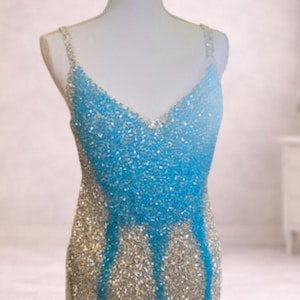 May include: A sleeveless dress featuring a V-neckline and thin straps, covered in a dense layer of shimmering sequins. The garment displays a color gradient transition from a bright, vibrant blue at the top to a metallic silver at the bottom.