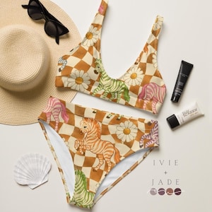 May include: A two-piece bikini set with a retro checkerboard pattern in shades of brown and cream. The bikini top and high-waisted bottoms feature colorful zebra illustrations and daisy accents. Sunglasses, a sun hat, sunscreen, and a seashell are also in the image.