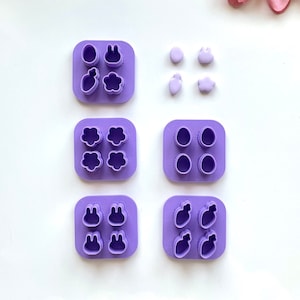 Puede incluir: Moldes de silicona púrpura para hacer decoraciones de fondant o arcilla polimérica. Los moldes presentan varios diseños con temática de Pascua, incluyendo conejos, huevos, flores y zanahorias.