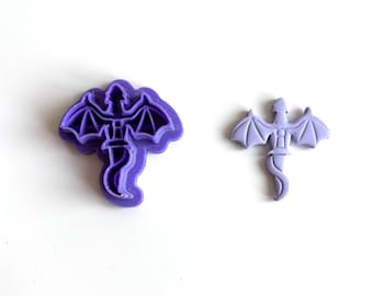 May include: Two purple dragon-shaped cookie cutters. One is a larger, detailed cutter with a winged dragon outline. The other is a smaller, simplified version of the same dragon design. Both are made of plastic and are on a white background.