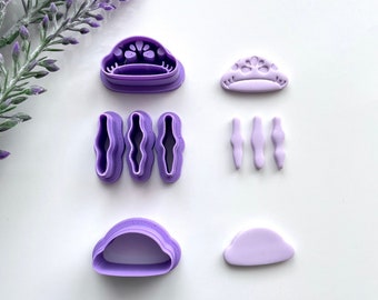 May include: Purple plastic cookie cutters in the shape of a cloud, a crown, and a flower. There are also three smaller cutters in the shape of a wavy line.
