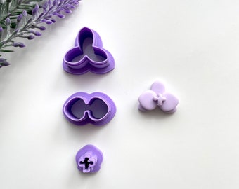 May include: Set of four purple plastic flower cookie cutters. The cutters are shaped like a flower with three petals, a flower with two petals, a flower with five petals, and a single flower center.