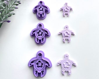 May include: Set of three purple plastic turtle cookie cutters, each with a different size. The turtles have a hibiscus flower design in the center.