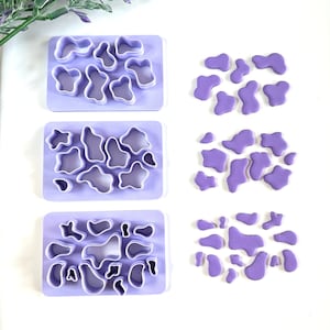 Peut inclure: Trois ensembles d'emporte-pièces en plastique violet en forme de formes organiques abstraites. Chaque ensemble est disposé en rangée sur une surface blanche. À côté de chaque ensemble se trouvent les formes découpées en fondant violet.