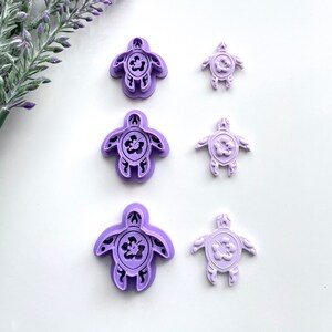May include: Set of three purple plastic turtle cookie cutters, each with a different size. The turtles have a hibiscus flower design in the centre.