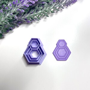 Könnte beinhalten: Ein Satz aus drei lilafarbenen Keksausstechern in Hexagonform. Die Ausstecher sind übereinander gestapelt, wobei der größte Ausstecher unten und der kleinste oben liegt.