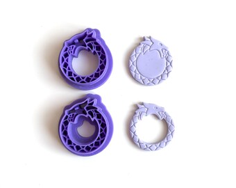 May include: Four purple dragon-shaped cookie cutters and stamps. Two are complete cutters, and two are stamps. The cutters have a detailed dragon design, while the stamps have a simpler dragon outline. The items are on a white background.
