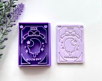 May include: Two purple polymer clay stamps with a moon and stars design. The left stamp says "Moon Sky" and the right stamp says "The Moon".