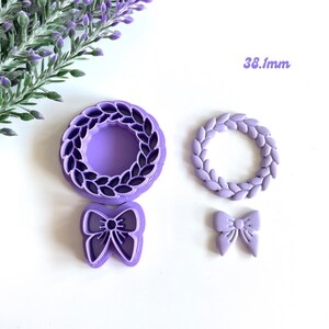 May include: A set of three purple plastic cookie cutters. The cutters are shaped like a wreath, a wreath with leaves, and a bow. The wreath cutter is 38.1 mm in diameter. The text "Available in bigger sizes" is printed below the cutters.