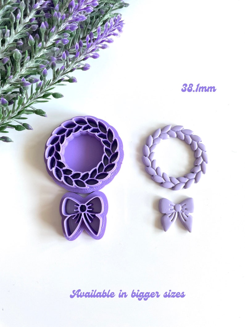 May include: A set of three purple plastic cookie cutters. The cutters are shaped like a wreath, a wreath with leaves, and a bow. The wreath cutter is 38.1 mm in diameter. The text "Available in bigger sizes" is printed below the cutters.