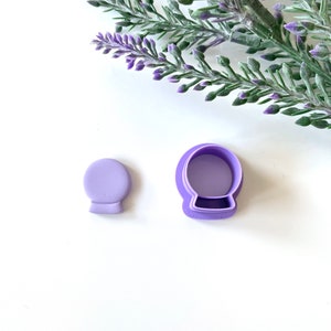 May include: Two purple plastic cookie cutters shaped like snow globes. The larger cutter is open and the smaller cutter is closed.