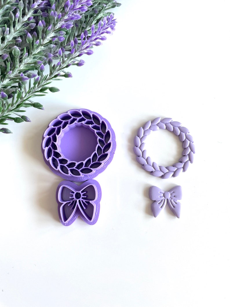 May include: A set of three purple plastic cookie cutters. The cutters are shaped like a wreath, a wreath with leaves, and a bow.