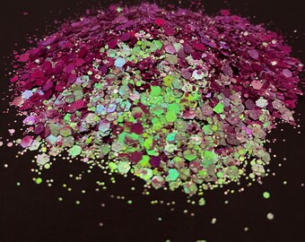May include: A pile of iridescent glitter with a mix of green and purple hues. The glitter is scattered on a black background.