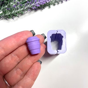 Könnte beinhalten: Eine violette Silikonform zum Herstellen einer kleinen Kaffeetasse. Die Form ist geöffnet und eine violette Kaffeetasse liegt daneben.