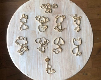 May include: A set of ten wooden animal and object cutouts, including a turtle, koala, frog, dog, cat, and a ball. The cutouts are all gold in color and are arranged on a light brown wooden surface.
