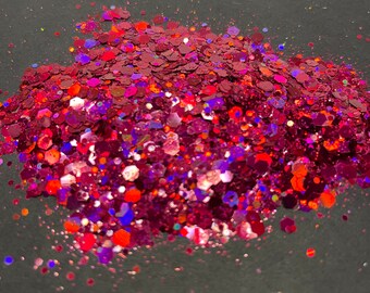 May include: A pile of red, orange, and purple glitter on a black background.