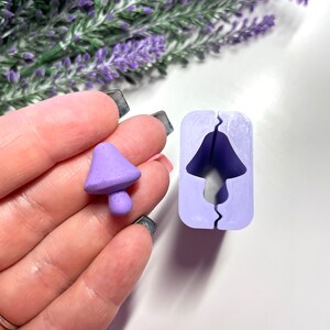 Peut inclure: Un moule en silicone violet pour la fabrication d'objets en résine en forme de champignon. Le moule est ouvert et un champignon en résine violet est placé à côté.