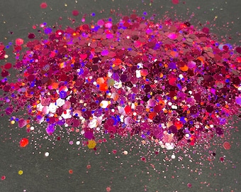 May include: A close-up of a pile of pink, red, and purple glitter on a dark gray background.