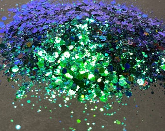 May include: A pile of iridescent green and blue glitter. The glitter is scattered on a gray surface.