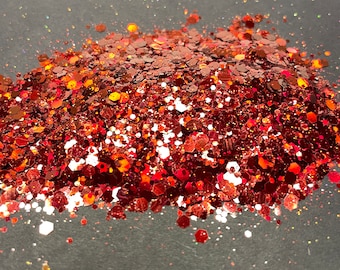 May include: A pile of red, orange, and white glitter on a gray background.