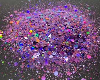 May include: A close-up of iridescent purple, blue, and green glitter. The glitter is scattered on a dark gray surface.