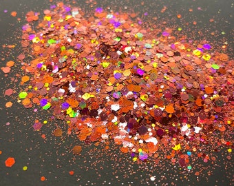 May include: A close-up of a pile of iridescent glitter in shades of red, orange, and gold. The glitter is scattered on a black surface.