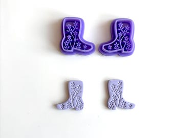 May include: Four purple boot-shaped cookie cutters. Two are a darker shade of purple and larger, with floral designs inside. The other two are a lighter shade of purple and smaller, also with floral designs. All are on a white background.