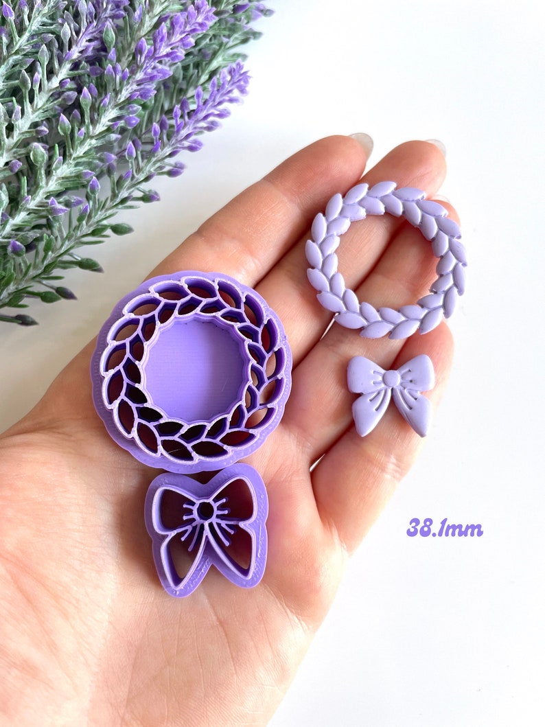 May include: A set of three purple plastic cookie cutters, featuring a wreath, a bow, and a wreath with a center cutout. The wreath is 38 mm in diameter.