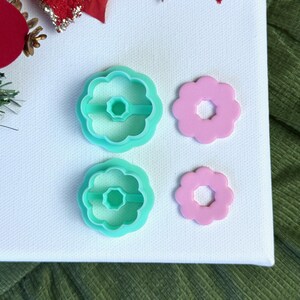 May include: Two sets of turquoise plastic flower cookie cutters with a pink flower cookie cutter in each set. The cookie cutters are on a white surface.