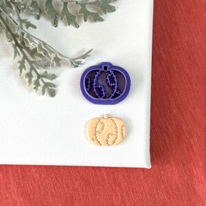May include: Purple plastic pumpkin cookie cutter with a detailed design and a matching tan pumpkin cookie.