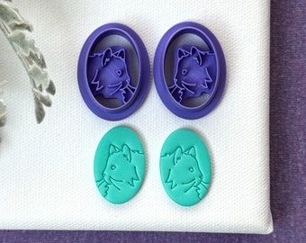 May include: Two purple plastic cat-shaped cookie cutters and two teal cat-shaped cookies.