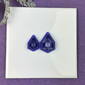 May include: Two purple plastic cookie cutters shaped like a geometric diamond with a hollow centre.