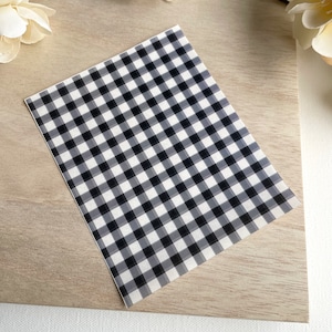 May include: A sheet of black and white gingham patterned vinyl. The vinyl is translucent and has a subtle sheen.