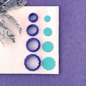 May include: A set of four circular scalloped cookie cutters in dark blue plastic, arranged in a vertical column. Beside each cutter is a corresponding teal scalloped circle shape, demonstrating the cut-out result of each tool in the set.