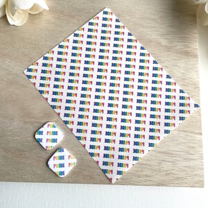 May include: Two square-shaped stickers with a rainbow "PRIDE" design on a white background. The stickers are on a wooden surface.